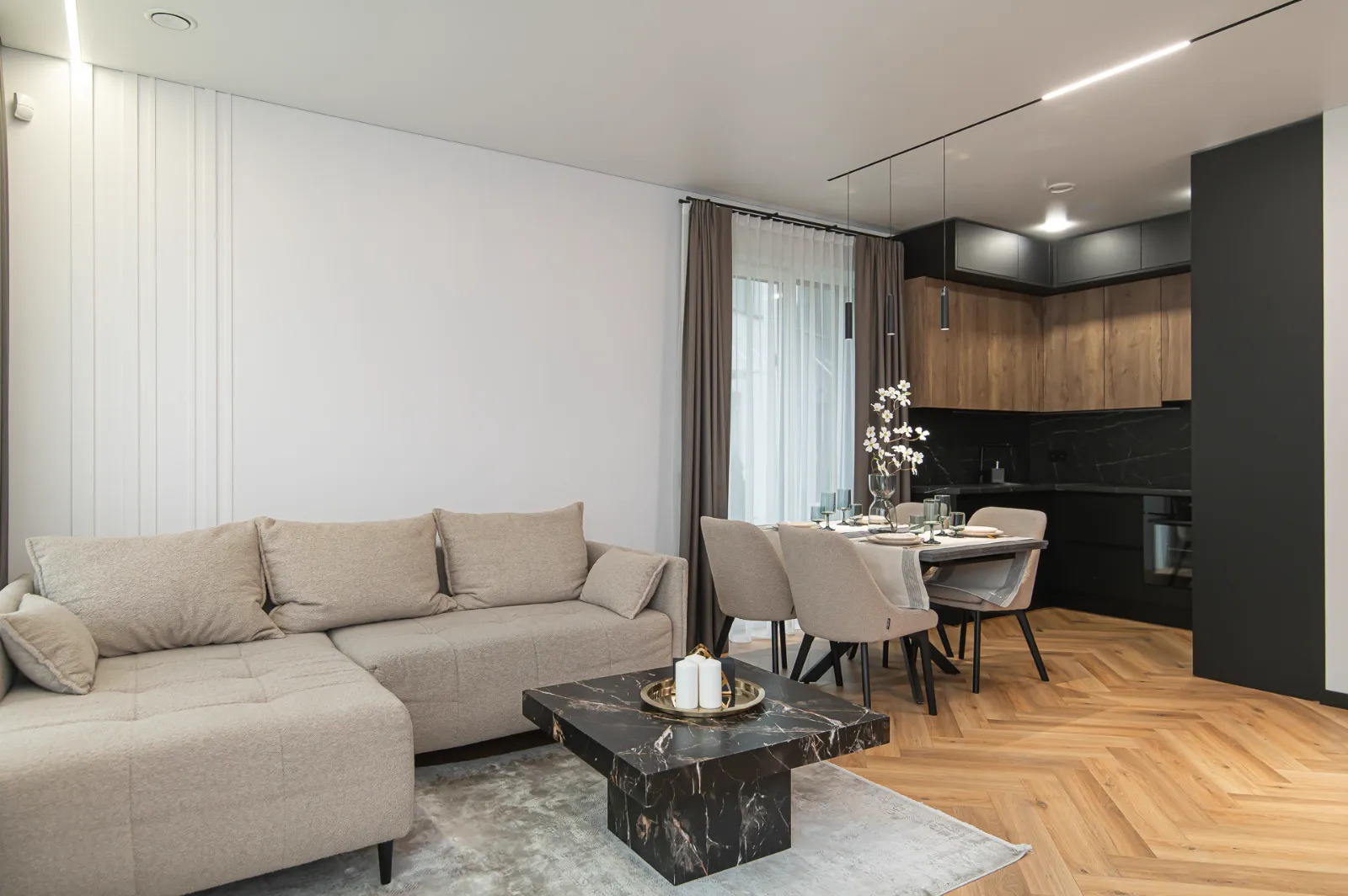 Šviesi svetainė su smėlio spalvos sofa ir eglutės parketu